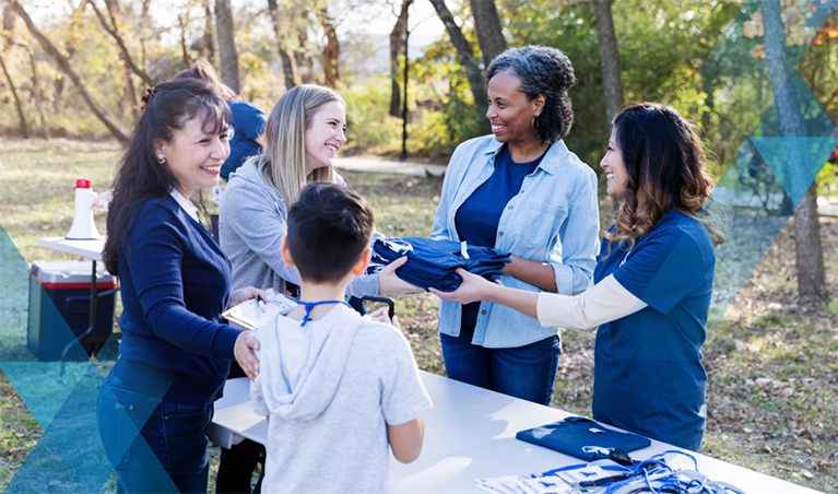 group of female and children volunteers smiling and exchanging tshirts around a table